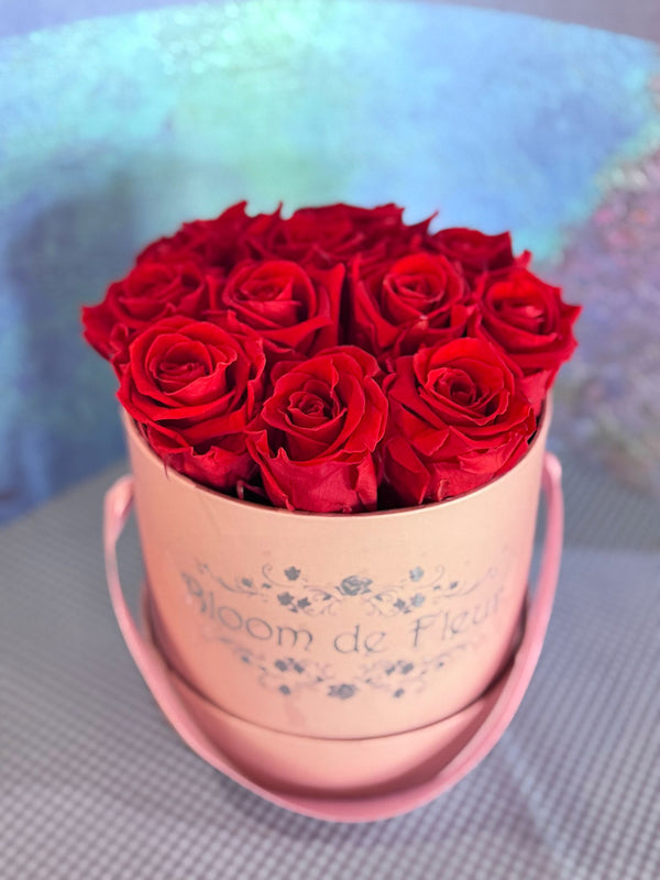 Light pink Bloom de Fleur hatbox with rope handles holding deep red roses.