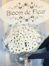 Bouquet of white daisy chrysanthemums with green centers wrapped in gray and blue polka-dot paper, tied with ribbon.