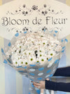 Bouquet of white daisy chrysanthemums with green centers wrapped in gray and blue polka-dot paper, tied with ribbon.