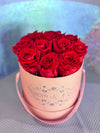 Light pink Bloom de Fleur hatbox with rope handles holding deep red roses.