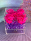 Clear acrylic cube box with drawer, featuring four hot pink preserved roses on top and purple crystal accents inside.