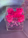 Clear acrylic cube box with drawer, featuring four hot pink preserved roses on top and pink crystal accents inside.
