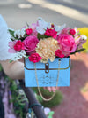 Light blue Bloom de Fleur purse box filled with pink roses, peach carnation, white orchid and filler flowers